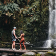 Load image into Gallery viewer, A couple stands in front of a waterfall on Hike & Seek 12 Apostles, Otways & Great Ocean Road day tour
